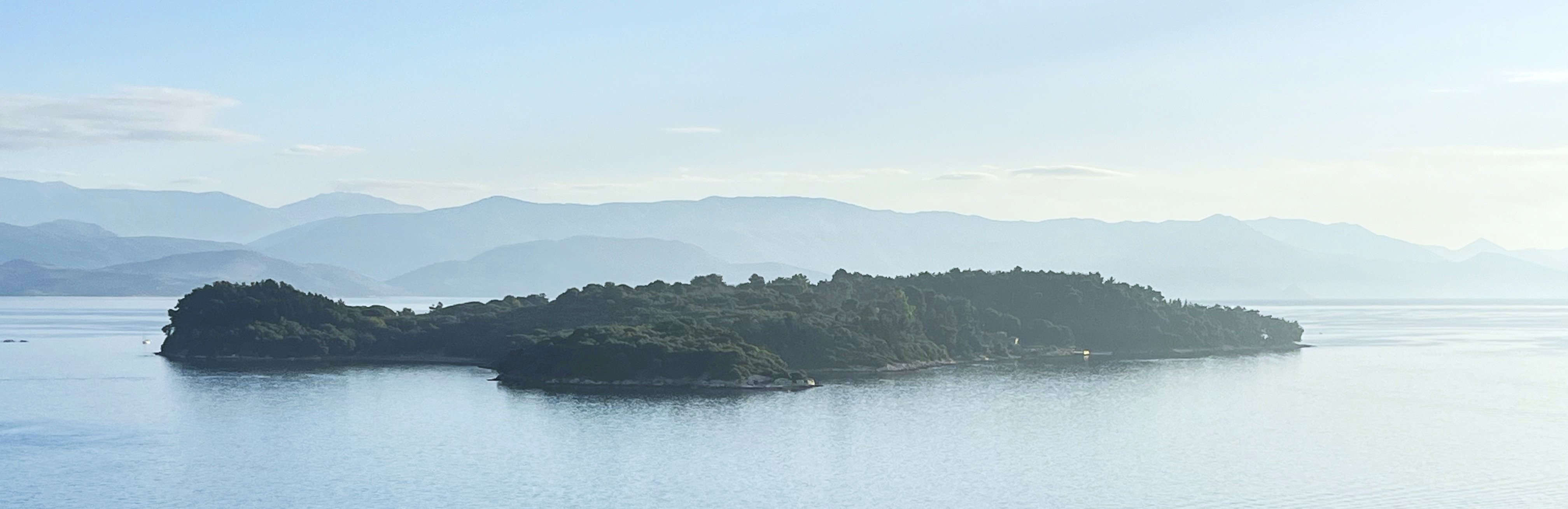 Bewaldete Insel in ruhigem Wasser vor einer Bergkette
