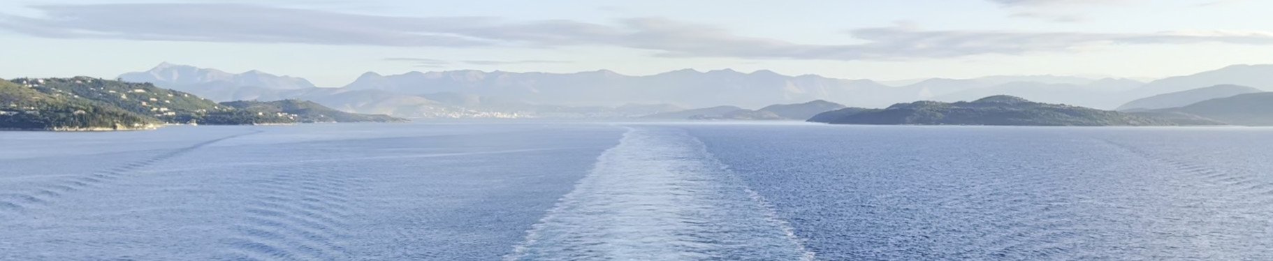 Scia di una nave su un mare calmo davanti a una costa con montagne